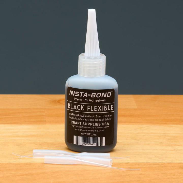 Insta-Bond black flexible adhesive bottle on a wooden surface with a dark background