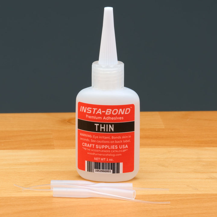Insta-Bond Thin glue bottle on a wooden surface with a dark background